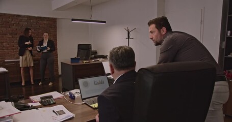 Multigenerational business associates collaborate on a project in an office. They discuss data analysis and business strategy. - Powered by Adobe