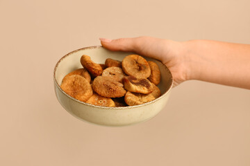 Female hand holding bowl with tasty dried figs on beige background