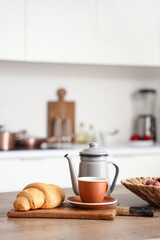 Kitchen table with teapot, cup of tea and croissant in modern kitchen