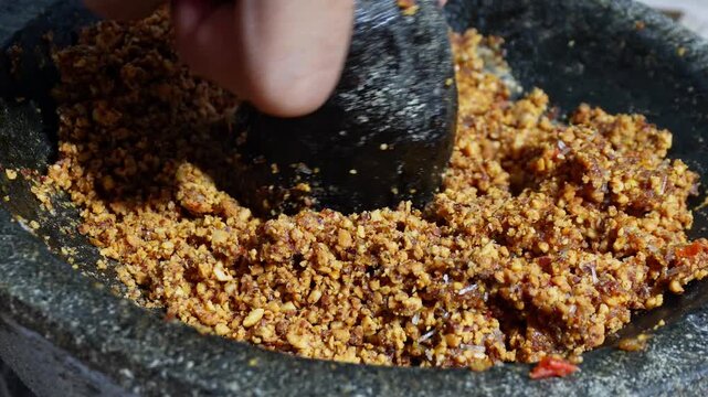 Homemade peanut chili sauce being ground in a stone mortar. Traditional Indonesian sambal making process with crunchy texture and bold flavors