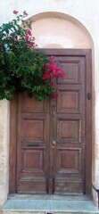 Fototapeta premium Rustic wooden door with an arched frame and vibrant Santa Rita bougainvillea blooms, perfect for décor, architecture projects, travel visuals, or designs seeking a warm, colorful Mediterranean touch.