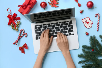 Female hands with laptop, Christmas decorations and gift box on color background