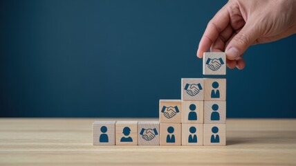 Human hand places wooden block depicting agreement atop ascending structure representing team building