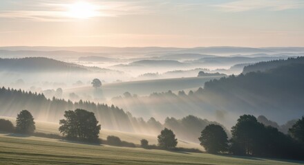 Misty morning landscape with sun rays breaking through fog over rolling hills and scattered trees at sunrise in the countryside
