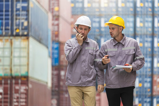 Logistics industrial workers communicating and inspecting cargo containers at port, Engineers discussing freight operations while using walkie talkie at shipping yard