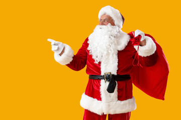 Santa Claus with Christmas bag pointing at something on yellow background