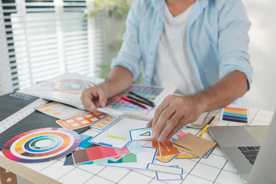 A designer is working on a creative UX UI project at a desk, arranging color palettes and layout templates with focus and precision, representing modern design and innovation.