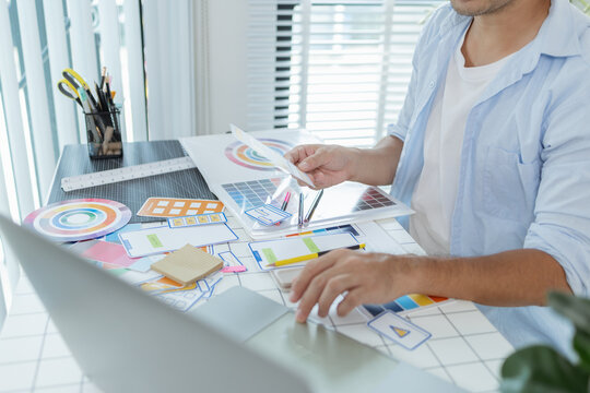A designer is working on a creative UX UI project at a desk, arranging color palettes and layout templates with focus and precision, representing modern design and innovation. - Powered by Adobe