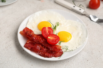 Plate with fried eggs, bacon and tomatoes on white background