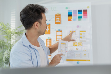 A focused designer is working on UX/UI design ideas, analyzing color palettes and interface structures pinned on a board. The scene reflects creativity, planning, and digital innovation.