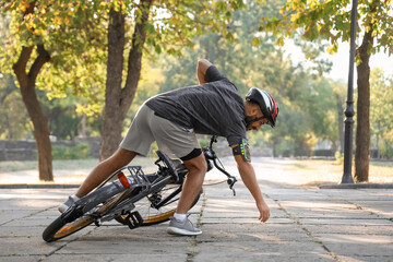 Young man getting up after falling off his bike in park
