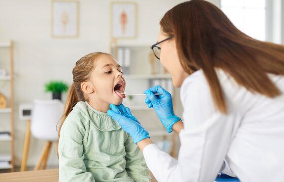 Dentist or doctor performing an oral, teeth or throat checkup on a child, girl patient in a clinic. Focus on dentistry, ENT care, and healthcare for proper teeth and throat inspection.