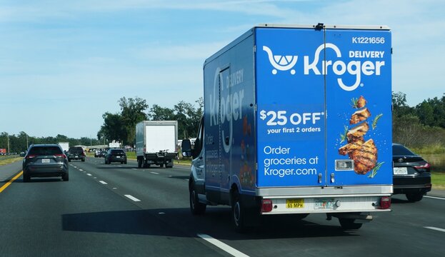 Tampa, Florida, U.S - Nov 10, 2025 - A Kroger delivery truck travels on a multi-lane highway under a bright, clear sky, featuring prominent advertising for online grocery ordering.