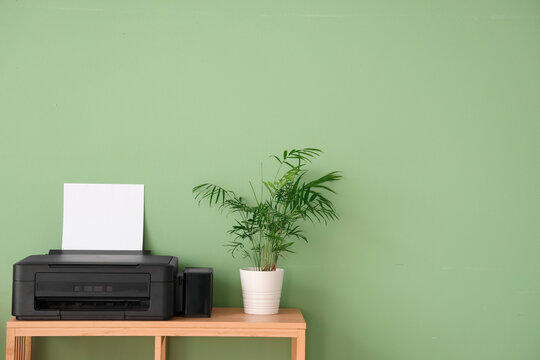 Stylish shelving unit with modern printer and houseplants near green wall
