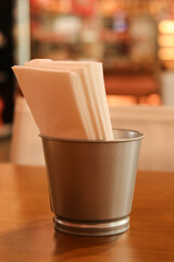 White paper napkin in metal container holder on wooden restaurant table, ready for dining. cozy background creates an inviting atmosphere for meal