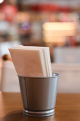 Metal bucket napkin holder with paper on wood table in cozy restaurant. warm, casual setting with blurred background perfect for food and drink concepts