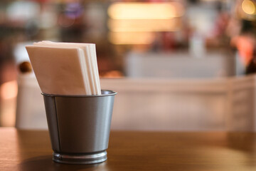 Metal cup holder with white paper napkins on wooden table inside cozy restaurant. blurred background creates calm and relaxed atmosphere for casual dining
