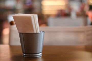Simple metal napkin holder with paper napkins on wooden table in cafe. warm, blurred background with bokeh creates quiet, calm, and waiting atmosphere