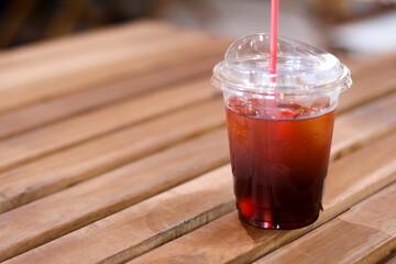 Refreshing iced coffee in clear plastic cup with red straw on wooden table. This cool cold brew americano drink relaxing choice for summer morning break at cafe