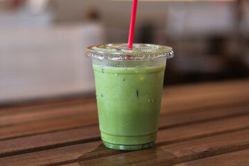 Delicious and refreshing iced matcha latte green tea beverage in clear plastic cup with red straw,...