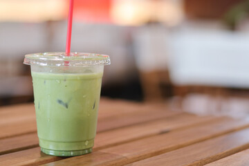 Refreshing iced matcha latte, cool green tea drink in plastic cup with straw, sits on wooden table in cafe, perfect beverage for calm afternoon