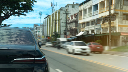 Rear side of luxury back car stop side of road. Blurred speed of car driving on the road with town under blue sky.
