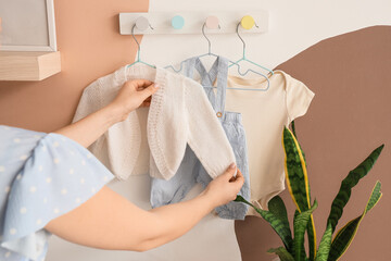 Obraz premium Pregnant woman with baby clothes hanging on wall at home, back view