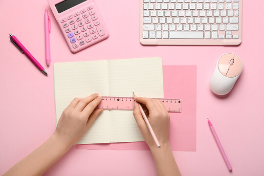 Female hands with pencil, ruler and open notebook on pink background
