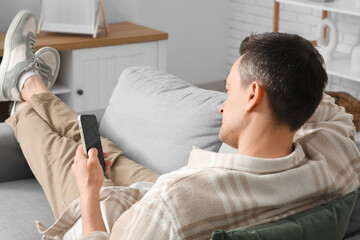 Obraz premium Young man using modern mobile phone with blank screen at home, back view