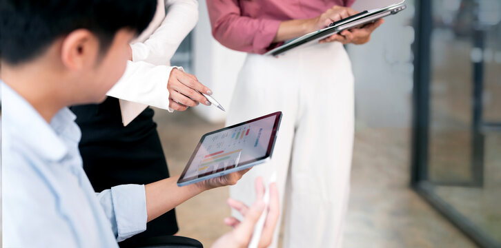 Close-up shot of three business professionals collaboratively analyzing financial data and charts displayed on a digital tablet during an office meeting.