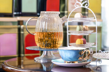 Glass teapot and blue teacup with macarons on a table