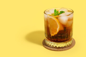 Glass of Long Island iced tea cocktail with mint on yellow background
