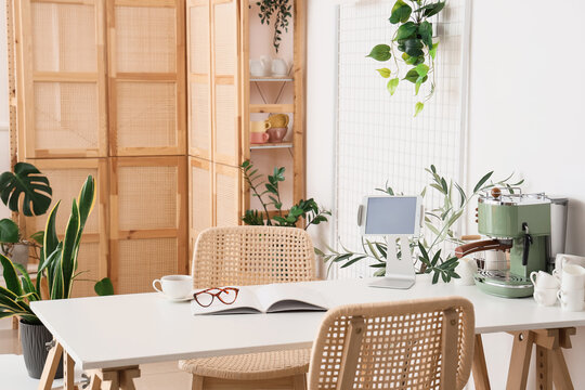 Interior of light kitchen with houseplants, modern coffee machine and tablet computer on table