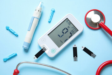 Glucometer, lancet pen, stethoscope and test strips on blue background. Diabetes concept