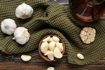 Bowl with fresh garlic cloves and jug of oil on wooden background