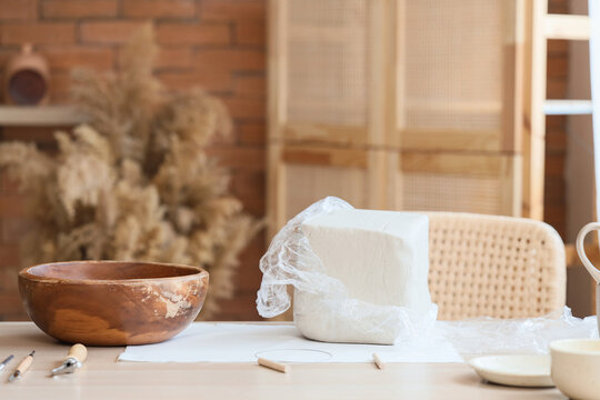 Wrapped clay block, bowl and pottery tools on table in home studio