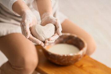 Young female potter holding heart made of clay in home studio, closeup