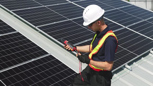 Technician installing solar panels on factory roof for green energy. A skilled technician in safety gear is working on a solar panel installation on rooftop. clean energy renewable power technology.