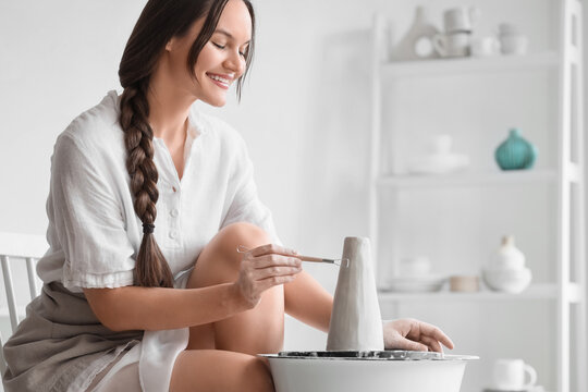 Young female potter shaping clay with loop tool on pottery wheel in home studio - Powered by Adobe