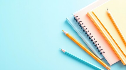 A close-up, top-down view of three pastel-colored notebooks stacked together and three pencils arranged on a solid pastel blue background. The lighting is brigh