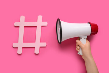 Female hand with loudspeaker and hashtag on pink background