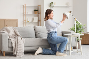 Pretty young woman changing light bulb of desk lamp in living room