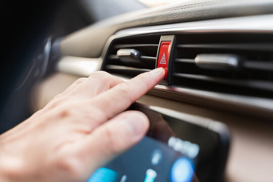 Hand pressing red hazard warning button inside modern car dashboard showing safety alert and emergency control