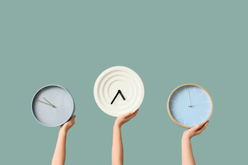 Female hands holding different wall clocks on green background