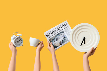 Female hands holding different clocks, newspaper and cup of coffee on yellow background