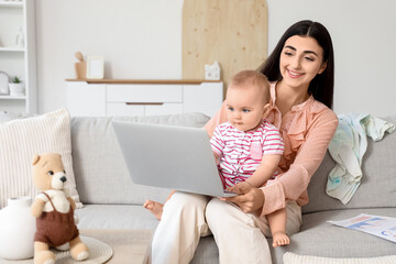 Young business mother and cute little baby working with laptop at home
