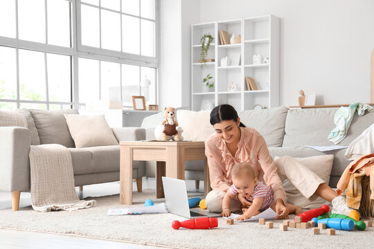 Young business mother working with laptop and cute little baby playing in living room
