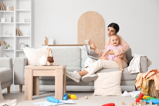 Busy young business mother with laptop, mobile phone and cute little baby at home - Powered by Adobe