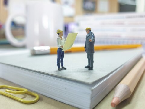 Mini toy of action figure at table with blurred background. Miniature photography concept design. Professional electrical engineer at office desk with book and pencil. Industrial concept.