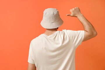 Handsome young man pointing at his stylish bucket hat on orange background, back view © Pixel-Shot